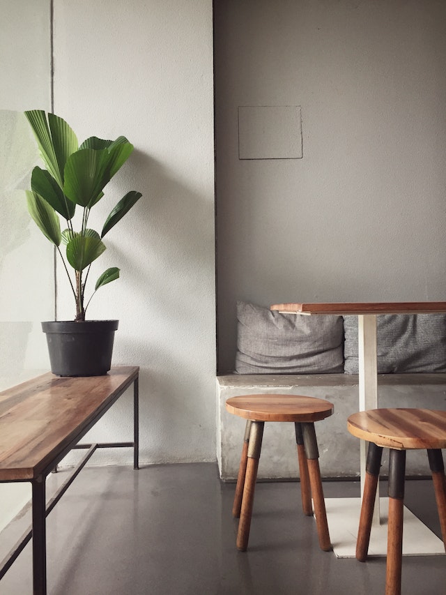 A living room showcasing wooden tables, chairs and a bench with a potted plant on top