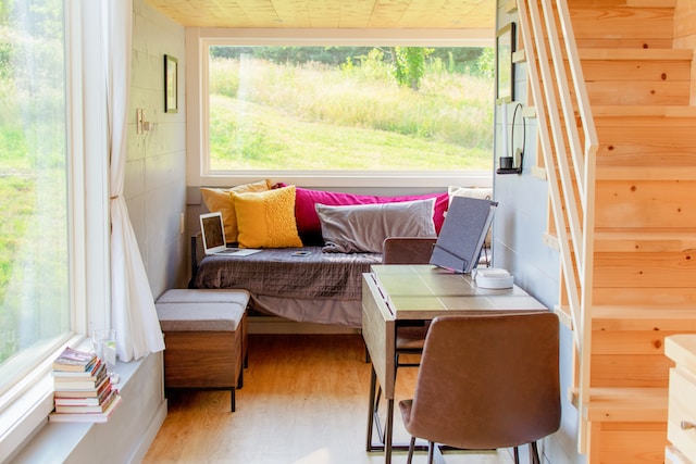 The interior of a tiny house showcasing both a lounge area and a multifunctional table with chairs that doubles as a workspace.