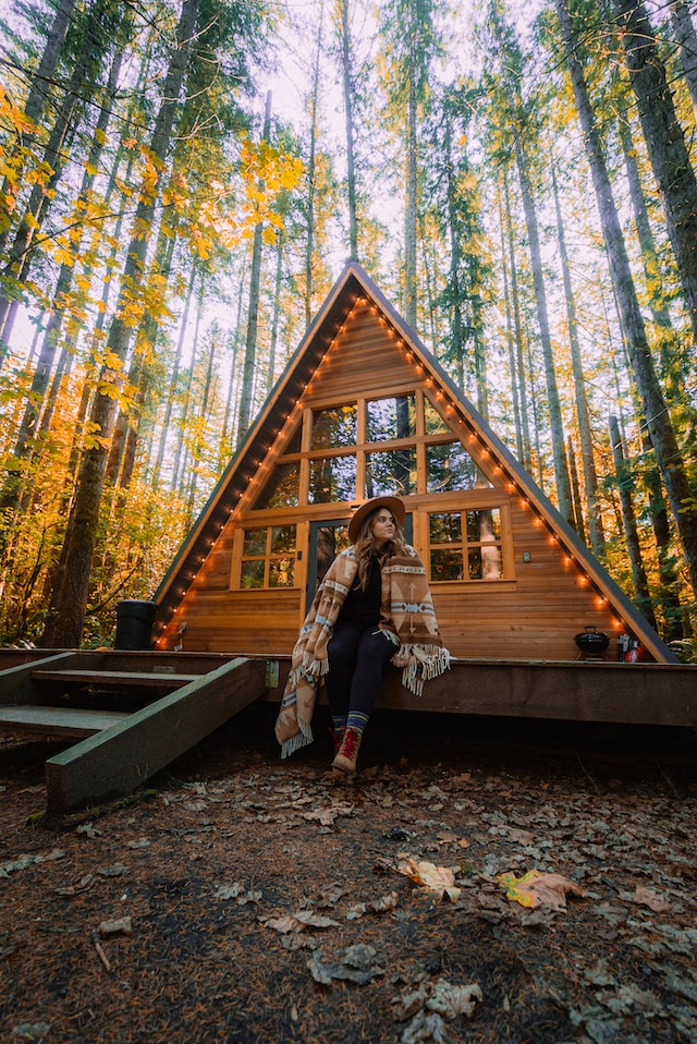 A woman sits outside a tiny house in the midst of trees