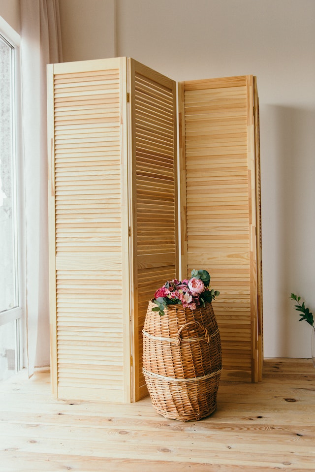 A wooden folding panel next to a rattan basket filled with flowers