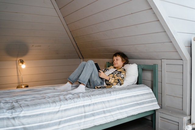 Boy reading a book on a bed in the attic