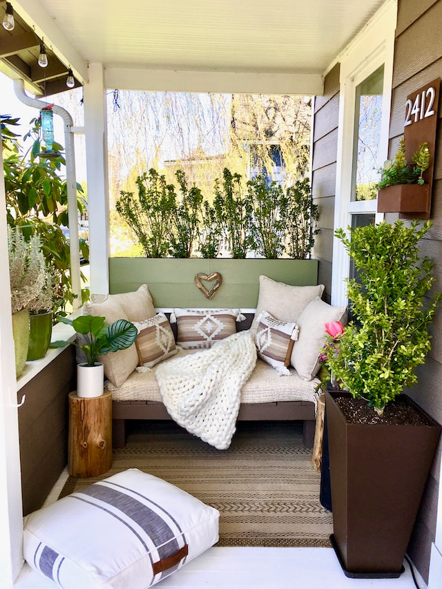 A balcony fitted with a love seat, cushions, and an assortment of plants
