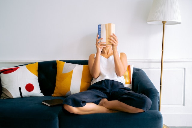 Woman sat reading on a dark blue couch with colorful throw pillows